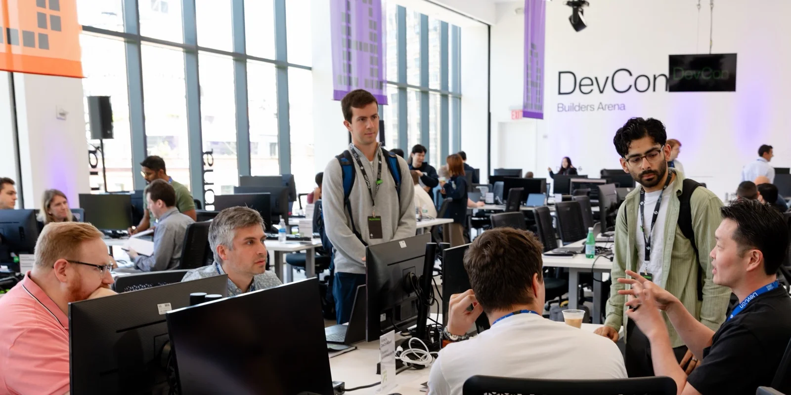 The DevCon Builders Arena: rows of workstations, people mid-build, and a conversation in progress at the right of frame.